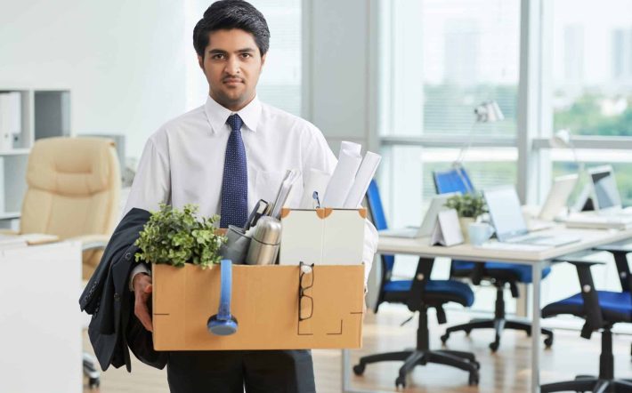 Portrait of Indian businessman with box with office stuff standing at office