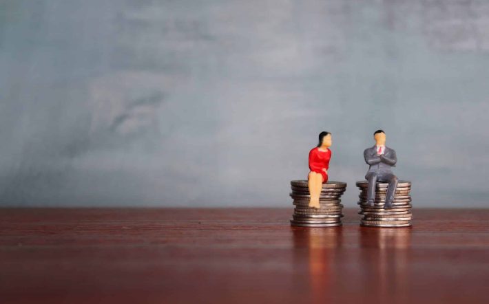 Concept of equal pay, Miniature man and woman sitting on a stack of coins with the same height. Copy space for text