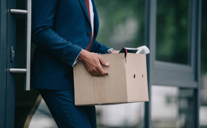 cropped view of fired businessman standing near building and holding carton box
