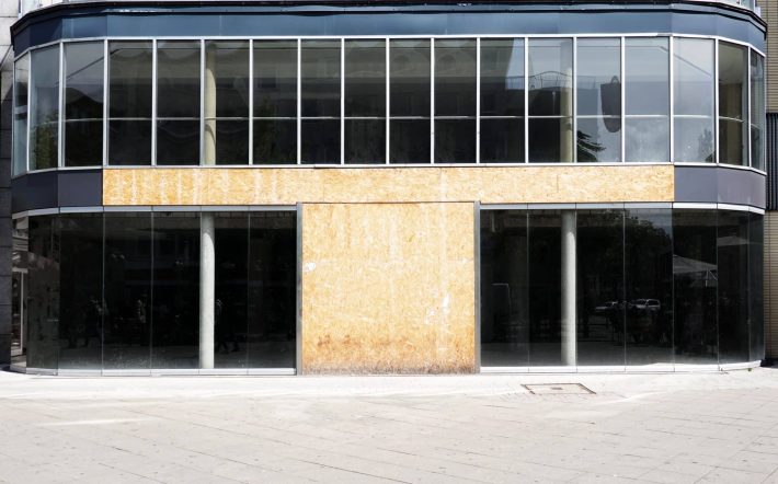 vacant commercial real estate with modern glass storefront boarded up after business closure